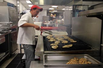 Photo of a chef cooking chicken breasts on a large grill.