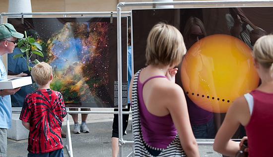 Photo of Farmers’ Market-goers looking at large displays depicting astronomical images.