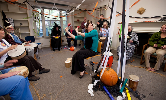 An associate outreach specialist plays maracas as other coworkers participate in a drumming circle, surrounded by Halloween decorations.