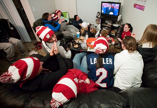 Photo of UW–Madison women's hockey team members gathered to watch the gold medal game, with coach Mark Johnson shown on TV.