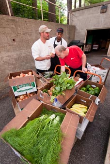 Photo of three UW Housing staff surrounded by boxes of peppers, squash, fennel, onions, tomatoes and other fresh produce.