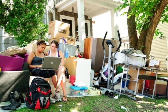 Photo of two students outside their apartment, surrounded by their belongings.