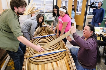 Photo: Valliere working on canoe with children watching